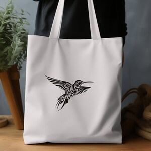 Puede incluir: Bolsa de lona blanca con un gr&aacute;fico de colibr&iacute; en blanco y negro. El colibr&iacute; est&aacute; estilizado con detalles intrincados.