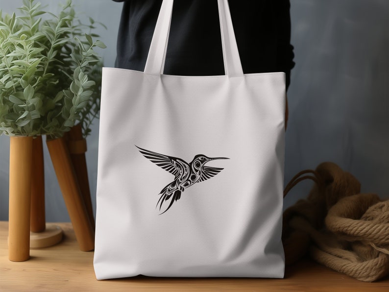 Puede incluir: Bolsa de lona blanca con un gr&aacute;fico de colibr&iacute; en blanco y negro. El colibr&iacute; est&aacute; estilizado con detalles intrincados.