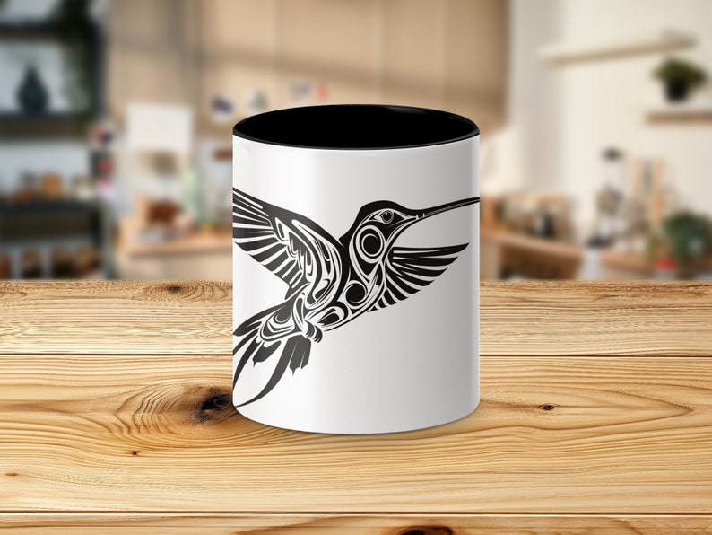Puede incluir: Una taza de cer&aacute;mica blanca con un borde y un asa negros. La taza presenta una ilustraci&oacute;n estilizada en blanco y negro de un colibr&iacute; en vuelo.
