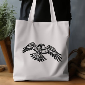K&ouml;nnte beinhalten: Wei&szlig;e Canvas-Tragetasche mit einer stilisierten Schwarz-Wei&szlig;-Illustration eines Vogels mit ausgebreiteten Fl&uuml;geln. Der Vogel ist im traditionellen indianischen Stil gehalten.