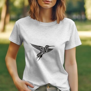 Puede incluir: Una camiseta blanca con un gr&aacute;fico de colibr&iacute; en blanco y negro. El colibr&iacute; est&aacute; estilizado con detalles intrincados y vuela hacia la derecha.