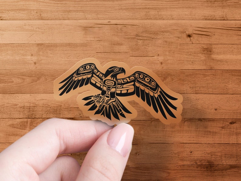 K&ouml;nnte beinhalten: Ein schwarzer und brauner Aufkleber mit einem stilisierten Adler mit ausgebreiteten Fl&uuml;geln. Der Adler ist im traditionellen Stil der amerikanischen Ureinwohner gehalten.