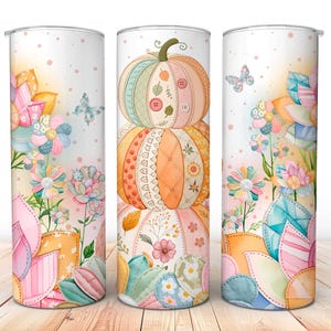 May include: A set of three white stainless steel tumblers with a watercolor design. The design features stacked pumpkins with button accents, flowers, and butterflies in pastel colors. The tumblers are decorated with a patchwork quilt theme.