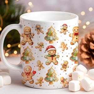 Op de afbeelding: Witte keramische mok met een feestelijk kerstontwerp. De mok is versierd met illustraties van peperkoekmannen, kerstbomen en gouden accenten. De handgreep is wit en de mok is gevuld met marshmallows.