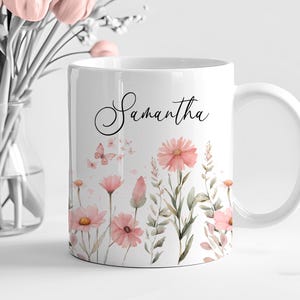 Può includere: Tazza in ceramica bianca con il nome "Samantha" in corsivo. La tazza è decorata con illustrazioni ad acquerello di fiori rosa, farfalle e vegetazione. Un regalo premuroso.