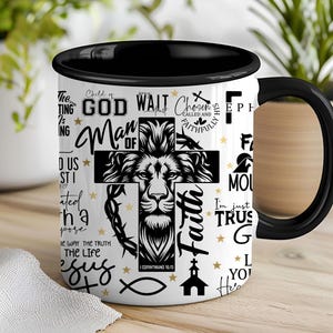 May include: White ceramic coffee mug with a black handle. The mug features a black and white graphic of a lion's head with a cross and the words "Child of God", "Man of Faith", "Wait", "Chosen", "Called and Faithfully", "I'm Just Trust", "The Way The Truth The Life", "Jesus", and "1 Corinthians 16:13".