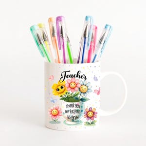 May include: A white ceramic mug with the word "Teacher" and a floral design, holding colorful gel pens. The mug features smiling flower illustrations and the text "thank you for helping us grow."