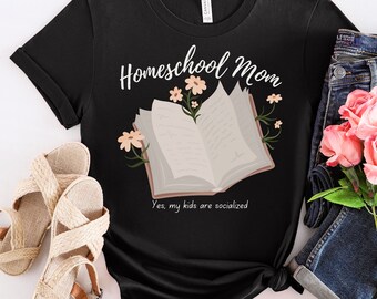 May include: Black t-shirt with the text "Homeschool Mom" and an illustration of an open book with flowers growing from it. The text "Yes, my kids are socialized" is below the book.
