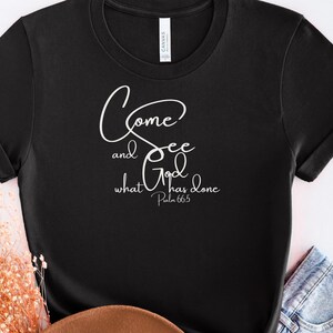 May include: Black t-shirt with the text "Come and See what God has done" in a white script font. The text is accompanied by the Bible verse reference Psalm 66:5. The shirt has short sleeves and a crew neck.