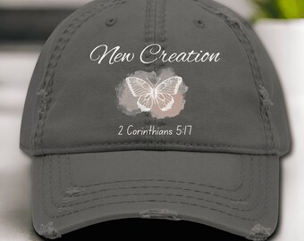 May include: A gray distressed baseball cap with a white butterfly graphic and the text "New Creation 2 Corinthians 5:17".