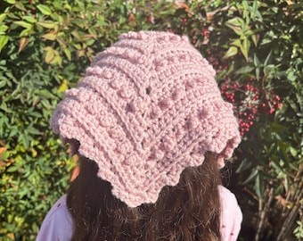 May include: A dusty pink triangular crochet headscarf featuring a textured bobble stitch pattern and a scalloped edge. The headscarf is crafted from yarn and displays a V-shaped design that tapers to a point at the back of the head.