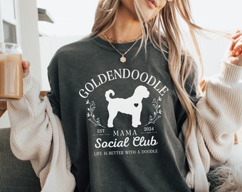 Può includere: Una felpa grigia antracite con un design grafico bianco che presenta un cane golden doodle, il testo "Goldendoodle Mama Social Club" e gli anni "EST. 2024".
