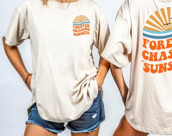 Puede incluir: Una camiseta beige con un gráfico de una puesta de sol y el texto "FOREVER CHASING SUNSETS" impreso en la espalda. La camiseta es de gran tamaño y tiene un ajuste holgado.