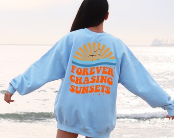 Puede incluir: Una sudadera azul claro con un gráfico de una puesta de sol y el texto "FOREVER CHASING SUNSETS" en naranja.