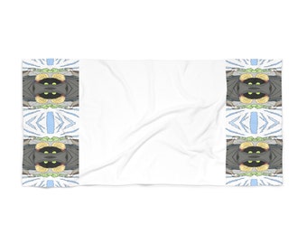 May include: A white beach towel with a colorful, symmetrical pattern of a creature with green eyes and yellow accents on the sides. The pattern is repeated along the sides of the towel.