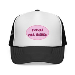 Puede incluir: Gorra de camionero en blanco y negro con visera curva. El panel frontal es blanco con un óvalo rosa que contiene el texto "FUTURE MRS. BIEBER" en morado. La gorra tiene una parte trasera de malla.