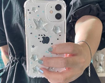 May include: A clear phone case with a glittery background and silver stars. The case has a raised design of silver stars and a blue glitter accent.