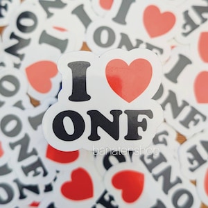 May include: A collection of white stickers with the text "I ONE" and a red heart. The word "ONE" is in black, and the heart is red. The stickers are scattered on a wooden surface.