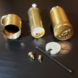 以下が含まれることがあります： ライター用の真鍮部品セット。芯ホルダー、バネ、ネジ、フェルトパッド、真鍮製のキャップが含まれています。キャップには「M.A.T.O.N. 1988」と刻印されています。
