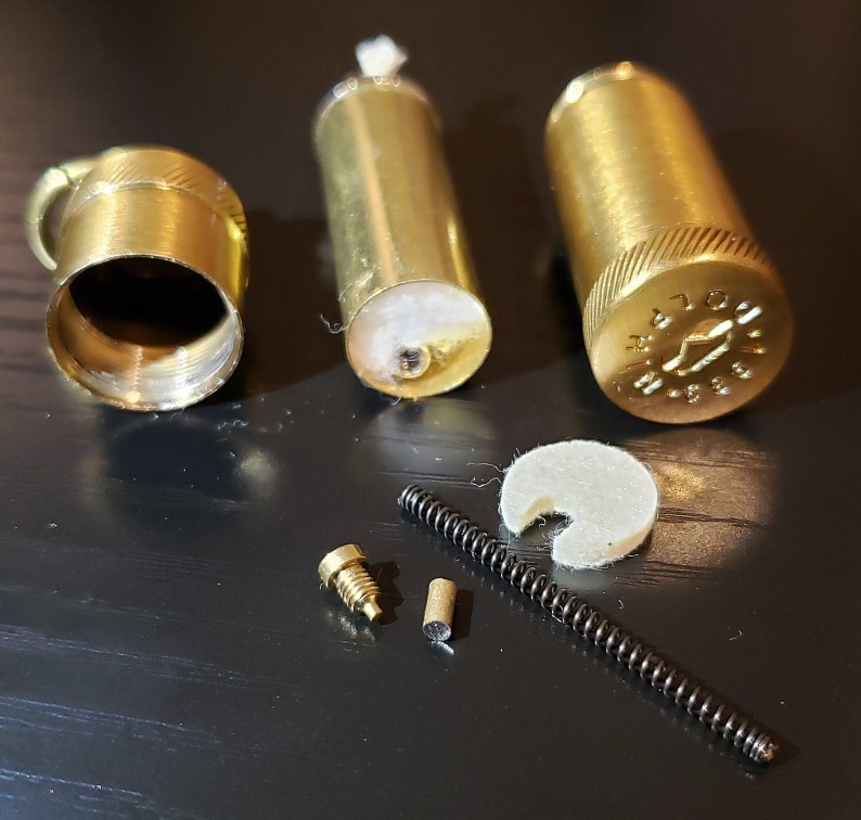 以下が含まれることがあります： ライター用の真鍮部品セット。芯ホルダー、バネ、ネジ、フェルトパッド、真鍮製のキャップが含まれています。キャップには「M.A.T.O.N. 1988」と刻印されています。