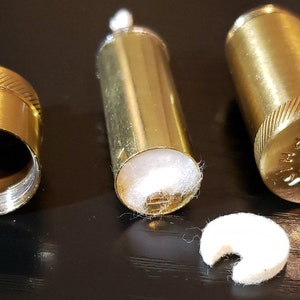 以下が含まれることがあります： 金色の金属製の容器が3つあり、中に白い綿の芯が入っています。容器は開いており、芯が見えています。右側の容器には芯が1つありません。