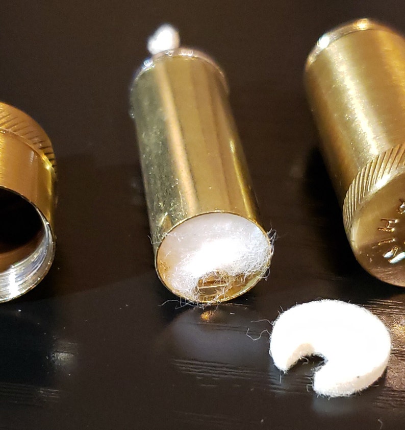 以下が含まれることがあります： 金色の金属製の容器が3つあり、中に白い綿の芯が入っています。容器は開いており、芯が見えています。右側の容器には芯が1つありません。