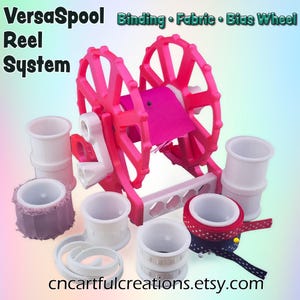 Puede incluir: Un sistema de carrete VersaSpool rosa con bobinas y accesorios blancos. El sistema incluye una rueda rosa para encuadernación, tela y rueda de sesgo. La imagen también incluye el texto "VersaSpool Reel System" y "Binding • Fabric • Bias Wheel". El sitio web es cncartfulcreations.etsy.com.