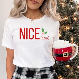May include: White t-shirt with red text that says "NICE (ish)" and a green holly leaf with red berries.