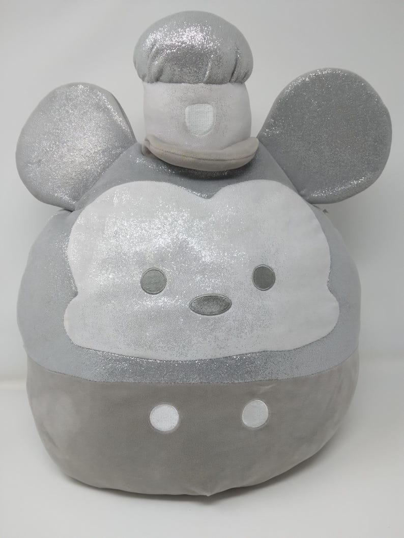 May include: A plush, round, gray character with large ears and a chef's hat. The character's face is white with gray eyes and a gray nose. The hat and ears have a glittery finish, and the bottom portion is a darker gray.