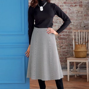 May include: A woman wearing a black turtleneck sweater and a black and white houndstooth skirt. She is standing in front of a blue door and a brick wall. She is wearing black boots.