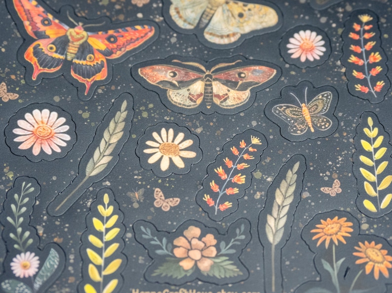 Puede incluir: Pegatinas decorativas con mariposas, flores y follaje en tonos naranja, amarillo y marr&oacute;n sobre un fondo oscuro. Las pegatinas tienen un aspecto texturizado y en relieve, con peque&ntilde;as motas doradas esparcidas.