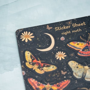 Puede incluir: Una hoja de pegatinas negra con tem&aacute;tica de polilla nocturna. La hoja presenta varias ilustraciones de polillas en tonos naranja, amarillo y marr&oacute;n, junto con una luna creciente y detalles florales. El texto "Sticker Sheet night moth" est&aacute; impreso.