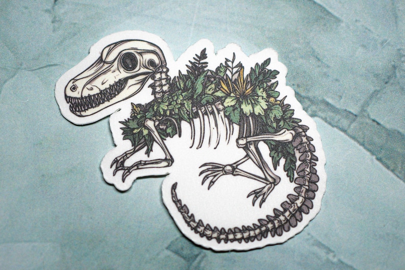 May include: A white sticker with a detailed illustration of a dinosaur skeleton with green foliage growing over the bones. The dinosaur is in a curled position with its tail wrapped around its body.