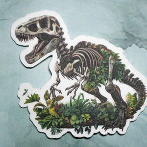 May include: A sticker of a dinosaur skeleton with green foliage growing over the bones. The dinosaur is in a crouching position with its head turned to the side. The sticker is on a light blue background.