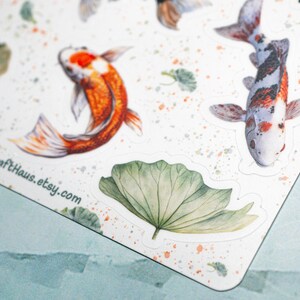 May include: A sheet of stickers featuring watercolor illustrations of koi fish and lily pads. The stickers are on a white background with a light orange splatter pattern. The text "HannaCraftHaus.etsy.com" is printed in the bottom left corner.