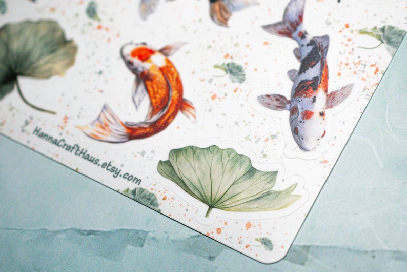 May include: A sheet of stickers featuring watercolor illustrations of koi fish and lily pads. The stickers are on a white background with a light orange splatter pattern. The text "HannaCraftHaus.etsy.com" is printed in the bottom left corner.