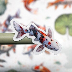 May include: A white, red, and black koi fish sticker with a white background. The sticker is on a gray surface.