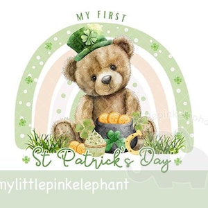 May include: A brown teddy bear wearing a green leprechaun hat holds a pot of gold with a shamrock and a horseshoe. The bear is sitting in front of a rainbow with green shamrocks on either side. The text "My First St. Patrick's Day" is written below the bear.