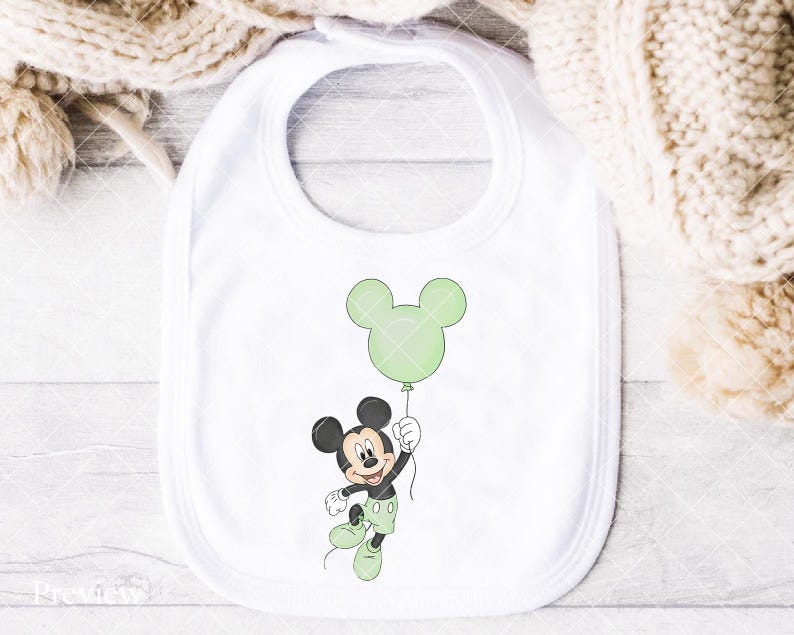 May include: A white baby bib with a cartoon illustration of Mickey Mouse holding a green balloon. Mickey is in black, white, and green, with a happy expression. The bib has a rounded shape and a neck opening for easy use.