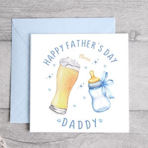 May include: A white card with blue text that reads "Happy Father's Day" and "Daddy". The card has a watercolor illustration of a glass of beer and a baby bottle with a blue bow.