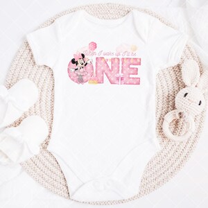 Puede incluir: Body de beb&eacute; blanco con el texto rosa "When I wake up I'll be ONE". El dise&ntilde;o incluye un gr&aacute;fico de Minnie Mouse. Tambi&eacute;n hay un par de patucos blancos y un juguete de conejo de ganchillo.
