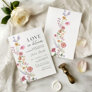 May include: Two white wedding invitations with floral designs and the text "Love in Bloom." The invitations feature watercolor flowers in pink, yellow, and purple. A gold wax seal and a rose are also visible.