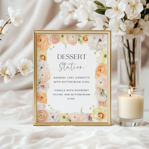 Puede incluir: Un letrero con marco dorado con las palabras "Dessert Station" y una lista de opciones de postres. El letrero está decorado con arreglos florales en tonos melocotón, blanco y amarillo. Una vela encendida está a la derecha.