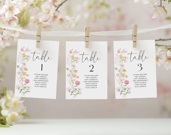May include: Three white table cards with floral designs and the word "table" in elegant script. Each card is numbered 1, 2, and 3, and held by wooden clothespins. The cards are decorated with pastel flowers.