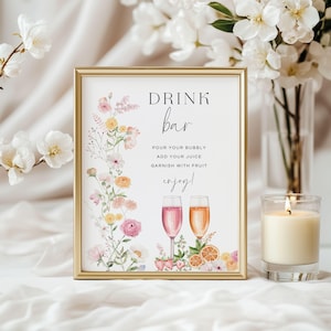 Könnte beinhalten: Ein goldgerahmtes Schild mit den Worten "DRINK bar" und Anweisungen für eine Getränkebar. Das Schild ist mit Blumenarrangements und zwei Sektgläsern verziert. Eine brennende Kerze und Blumen sind im Hintergrund.