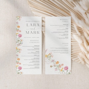 Könnte beinhalten: Ein Hochzeitsprogramm mit floralen Akzenten. Auf der linken Seite steht "Willkommen zur Hochzeit von Lara und Mark" mit Datum und Ort. Die rechte Seite listet die Details der Hochzeitsgesellschaft auf. Zarte Aquarellblumen in Rosa, Gelb und Orange schmücken die Ränder.