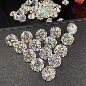 May include: A collection of round, clear gemstones with brilliant facets, arranged on a black surface. The gems reflect light, displaying a rainbow of colors. Some gems are scattered in the background, while others are arranged in a triangular pattern.