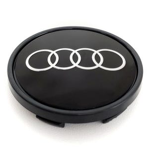 May include: Black car wheel center cap with the Audi logo. The logo features four interlocking silver rings on a glossy black background. The cap has a black outer ring and a slightly raised profile.