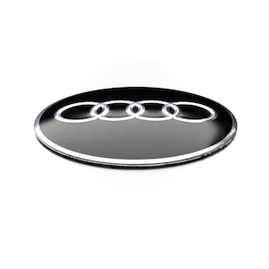 May include: A black and silver Audi emblem on a round, black background.