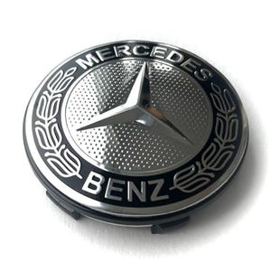 May include: A silver and black Mercedes-Benz emblem. The emblem features the Mercedes-Benz logo, a three-pointed star, in the center. The words "MERCEDES" and "BENZ" are inscribed around the star.